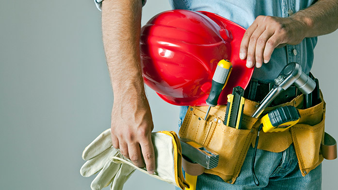 Handyman holding gloves and a red hardhat and wearing a fully equipped utility belt