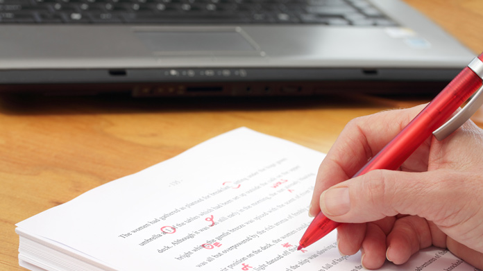 Hand holding a red pen making corrections to a printed document