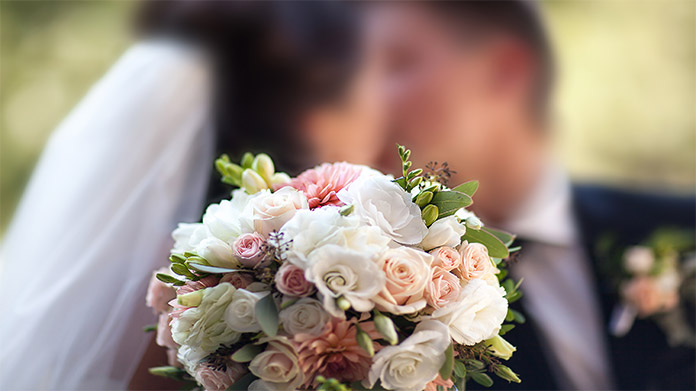 Photo of a bride and groom kissing behind a bouquet