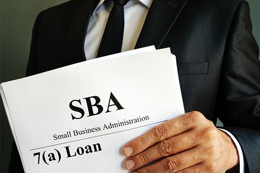 Man holding a stack of paper with "SBA 7(a) loan" on the front