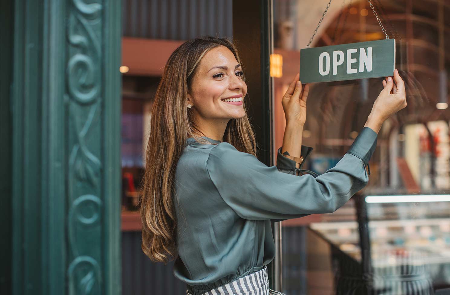 Woman smiling, turning shop sign to Open